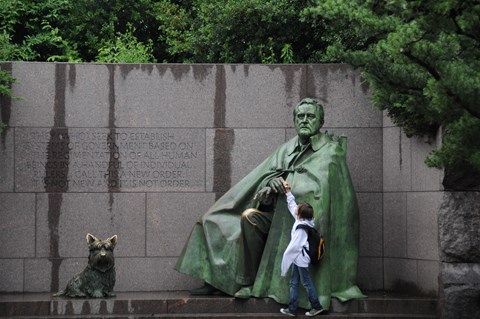 A child reaches up to touch a large bronze statue of Franklin Roosevelt.