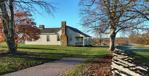A historic farmhouse is bordered by trees and a wooden split-rail fence