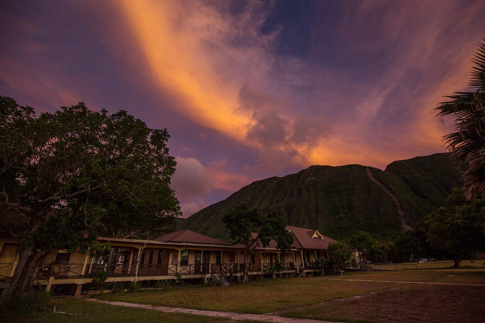 A vibrant and colorful sunset above a few buildings all connected by a covered walkway.