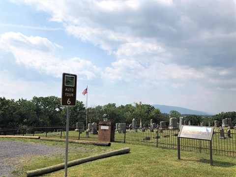 A road sign labeled auto tour 6 marks a tour stop and exhibit by a cemetery.