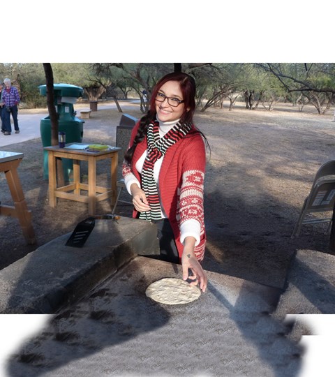 young woman flipping a flour tortilla on an open comal