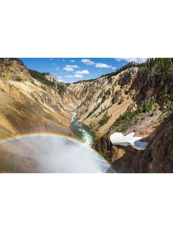 A rainbow is cast in the mist from a waterfall over a river that cuts through a deep canyon.