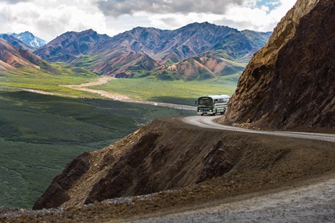a green colored bus traveling a dirt road on a mountainside