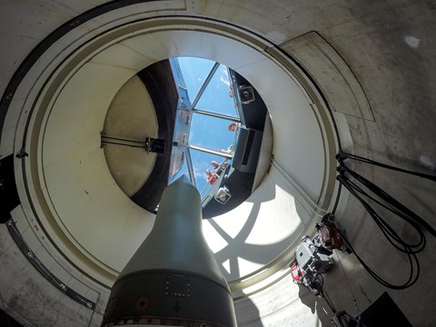 Park ranger and visitors look through a glass barrier at a missile standing in a missile silo