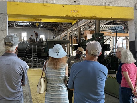 A ranger is shown speaking to a crowd of visitors while in a mechanical shop