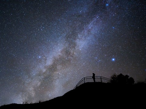 The black silhouette of a person standing at a viewpoint with the milky way in the backgroundn