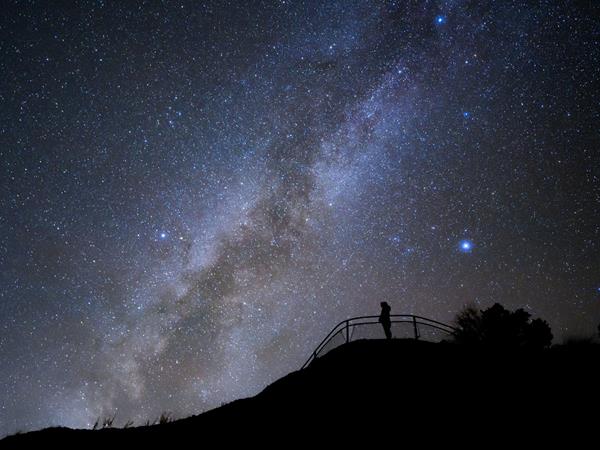 The black silhouette of a person standing at a viewpoint with the milky way in the backgroundn