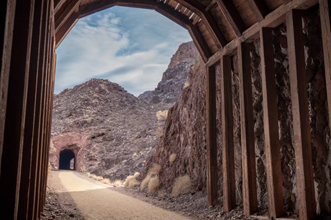 A tunnel constructed of wood beams looking out down a trail towards another tunnel.