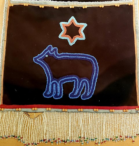 Beaded bag with a blue outline of a bear and orange six pointed star above.