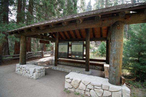 A brown roof stands over a wooden panel. On the panel is information about trails