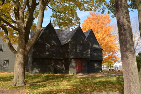 Large gray three story building with red door surrounded by green and yellow trees.