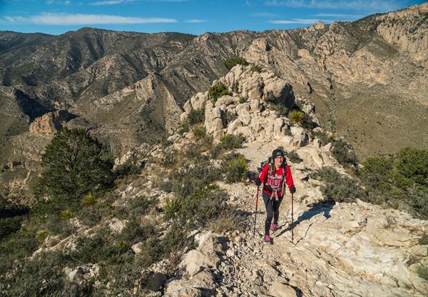 a woman with hiking poles ascents a mountain trail