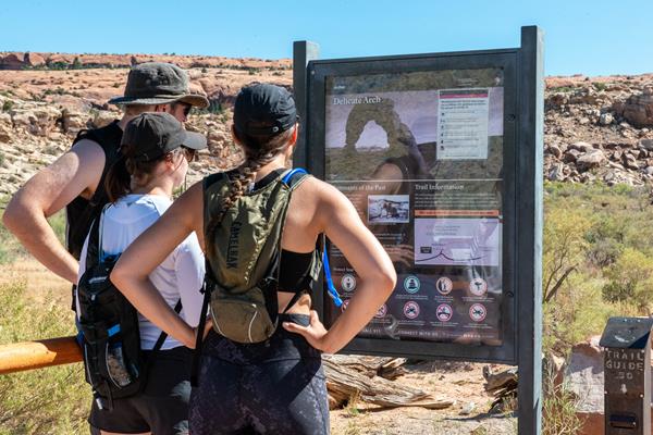 Visitors read the Delicate Arch Trailhead panel before embarking on a hike.