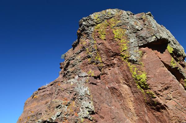 A tall reddish-brown rock pillar is spattered with yellow, white, and orange lichen.