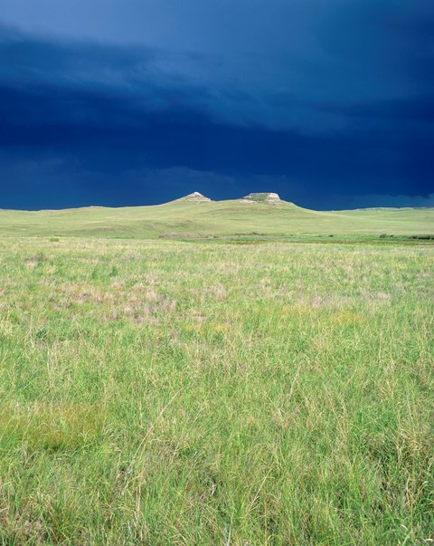 The sun illuminates the fossil hills with a dark, stormy sky in the background.