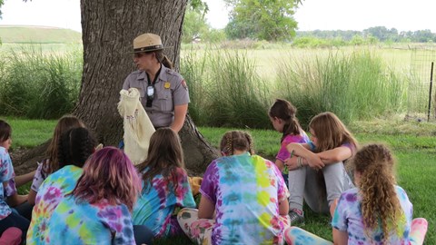 A ranger holds a tanned animal hide in front of a group of children.