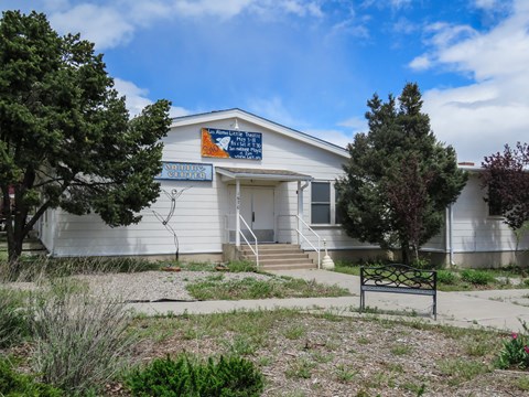 A wooden, white building with a blue and orange sign with white text.