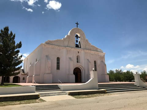 A tan, spanish-colonial style mission stands under a blue sky.