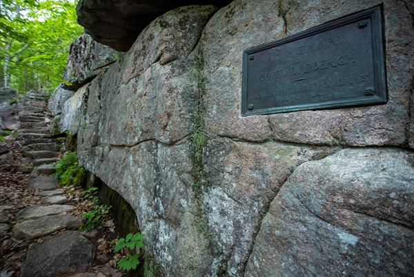 Looking up a trail of stone steps a large bronze plaque is embedded in a large granite rock