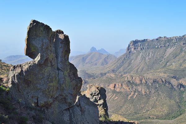 A large rock formation juts above the surrounding terrain and distant mountains loom behind it.