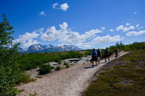 Several hikers along a path with mountains in the background