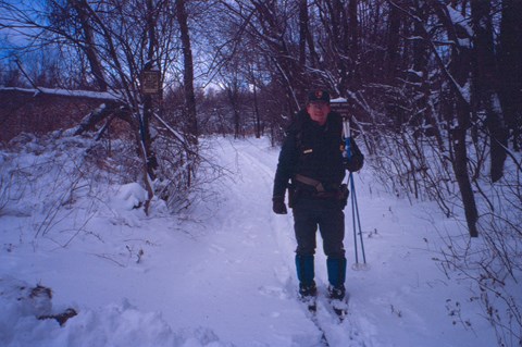 A park ranger in green uniform, skiing along a snowy forest trail.