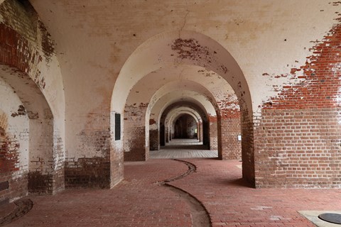 Interior of a brick structure with thick walls, arches separate several rooms.