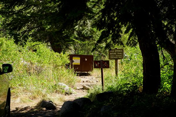A brown sign with text on it stands next to a dirt trail