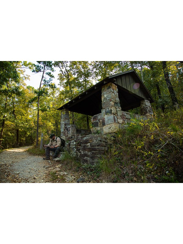A stone shelter built in a 1930s style sits alongside a gravel trail.