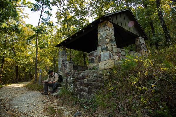 A stone shelter built in a 1930s style sits alongside a gravel trail.