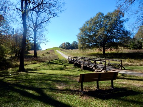 A park bench overlooking the paved main trail leading towards the Earth Lodge.