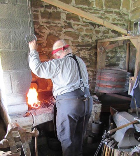 Man in 19th century clothes working over a blacksmith's forge.