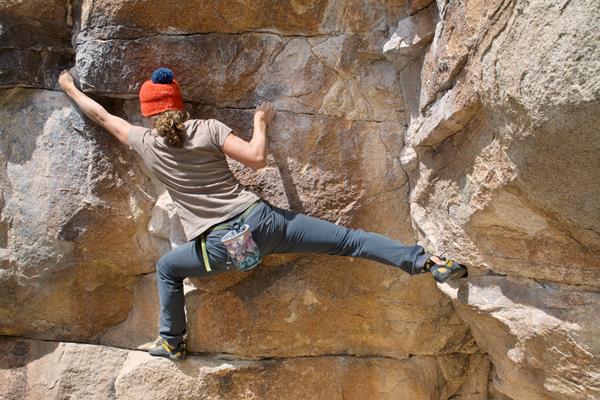 A boulderer stretching as the climb across a large rock face