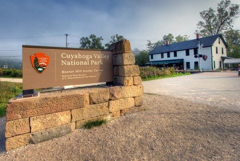 Sign with stone base reads "Cuyahoga Valley national Park," a white two-story building behind it.