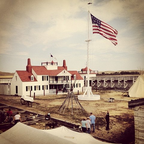 Large American Flag flys in front of Ornate House with visitors walking in fort courtyard.