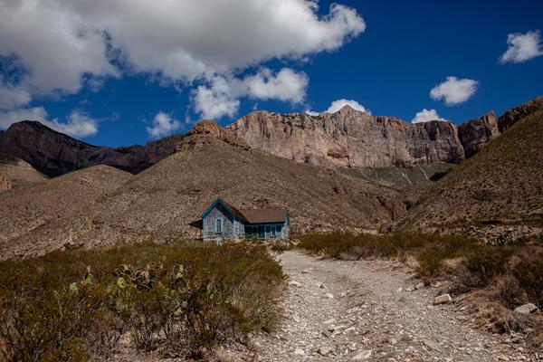 A wood frame home sits below tall limestone mountains