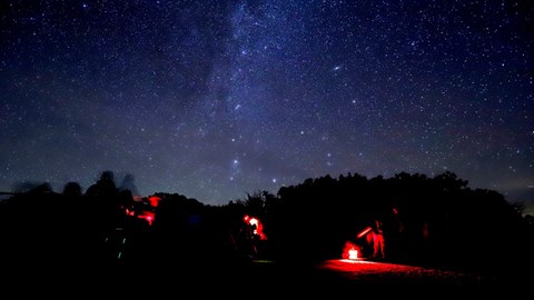 People standing around telescopes with red headlamps underneath a night sky
