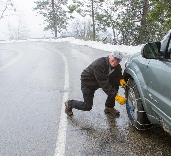 A man smiles at the camera as he finishes installing tire chains