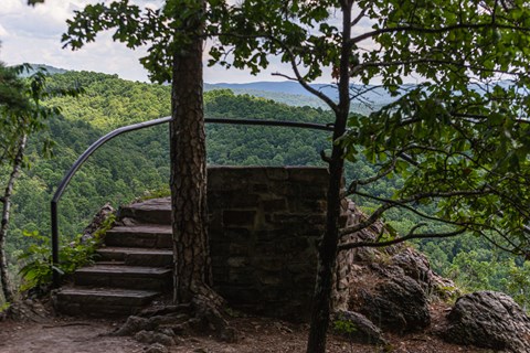 A black metal rail surrounds an outcropping overlooking rolling, forested hills.