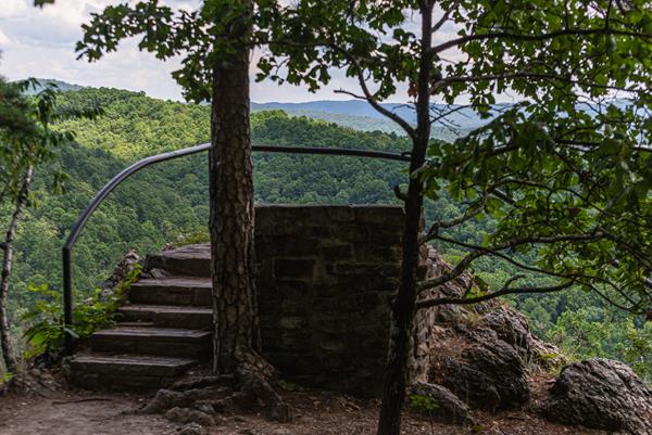 A black metal rail surrounds an outcropping overlooking rolling, forested hills.