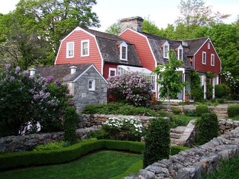 A red house with a stone wall and flowers around it.