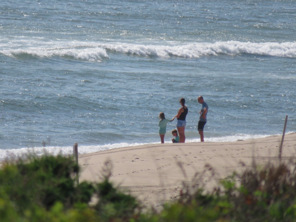 A man, woman, and two children stand together on the beach as the waves roll in.