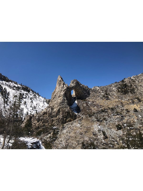 Large tan limestone arch with snow on the ground.