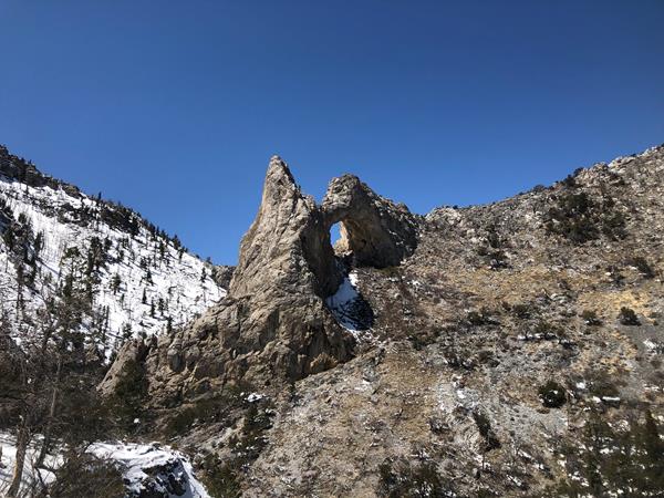Large tan limestone arch with snow on the ground.