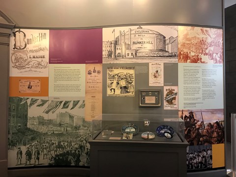 A wall of an exhibit filled with images and text. A glass case of artifacts sits in front.