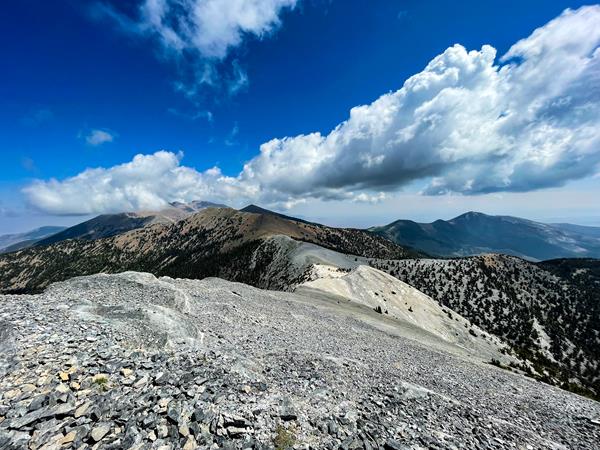 a bare alpine ridge with blue sky and white puffy clouds above.