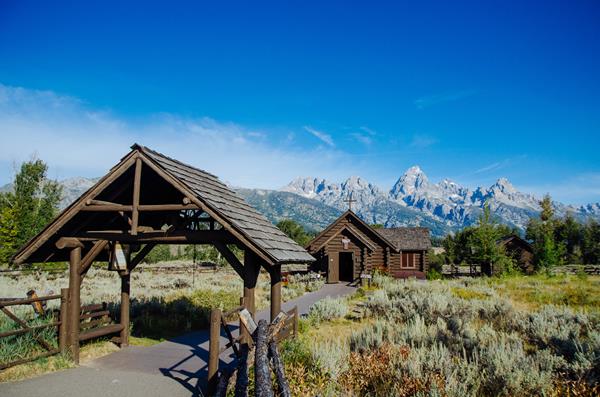 A log chapel in front of mountains.