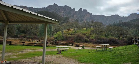 Shade structure and two picnic tables set before rock formations peering out of fog in winter