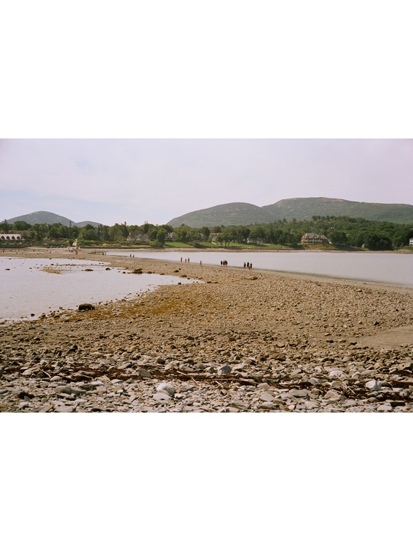 People walking across an exposed sand bar between an island and the mainland