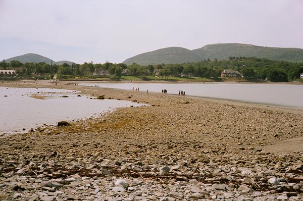 People walking across an exposed sand bar between an island and the mainland